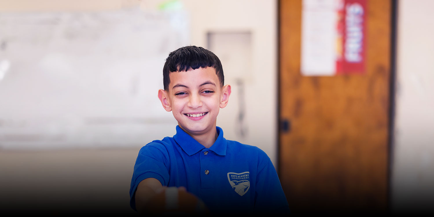 Smiling student wearing a Northwest Academy polo holding a football in a classroom.